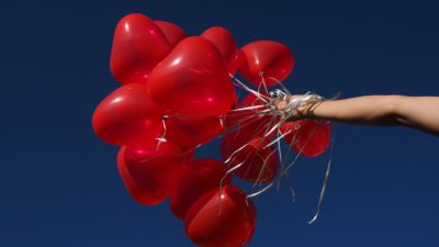 Bild på en hand som håller i ett tjugotal ballonger formade som hjärtan.