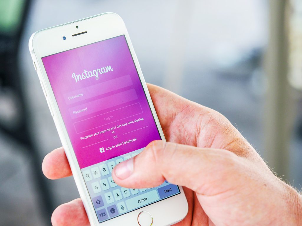Bild på en hand som håller i en mobil. På displayen syns Instagrams förstasida.